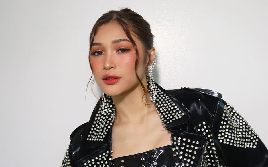 BINI Jhoanna posing with confidence in a studded black leather jacket and corset top, paired with a textured red skirt.