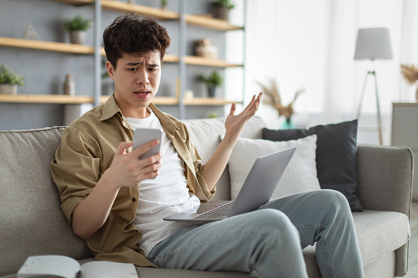 Confused Asian man looking at smartphone with a scam message.