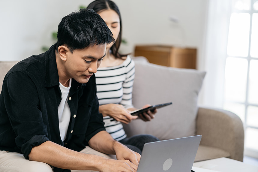 Photo of a man researching on his laptop with his wife beside him.