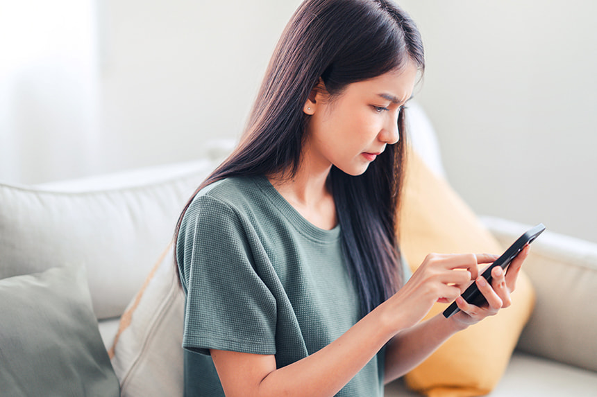 Young Asian woman using her smartphone to report a text scam.