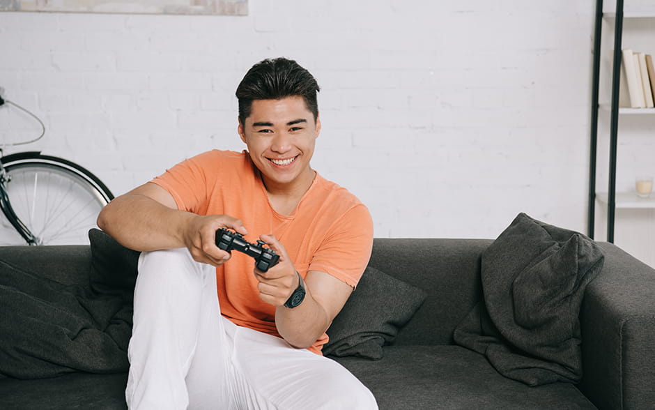 A young Asian man holding a controller and playing a video game at home.