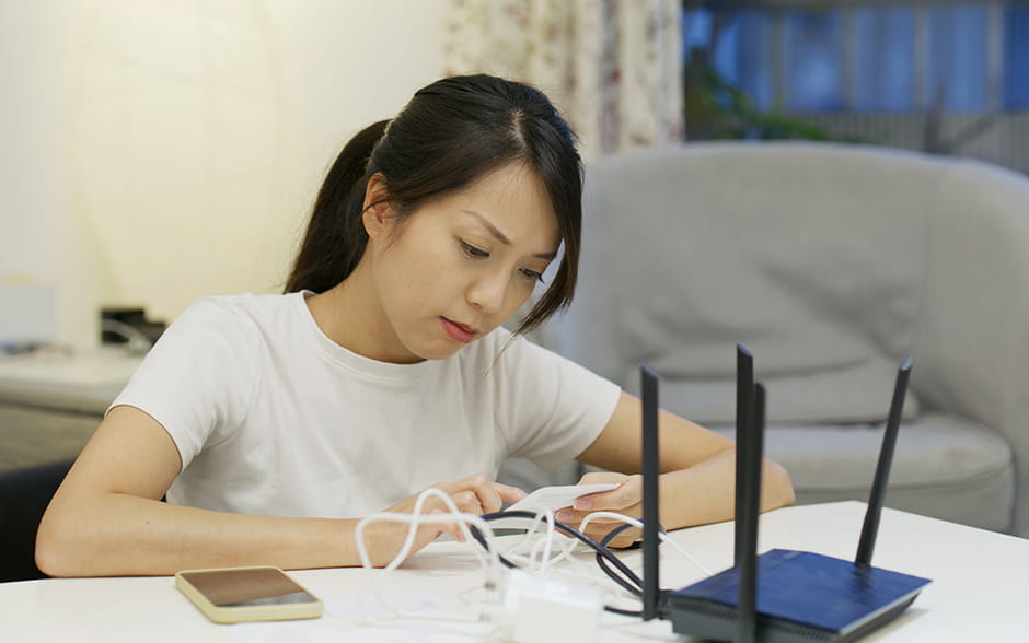 A young Asian woman reading instructions on how to connect the cable to a WiFi router.