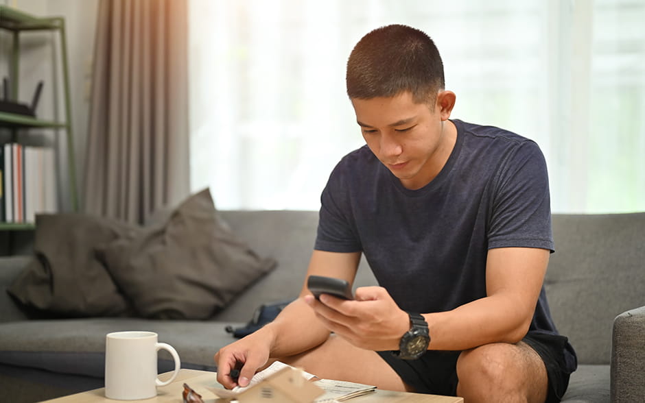 Asian man looking at his phone at home on the couch.