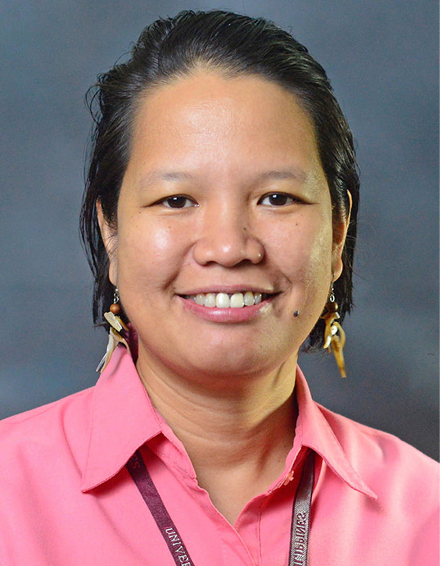 A woman wearing a pink shirt and earrings, smiling softly, with a neutral background.