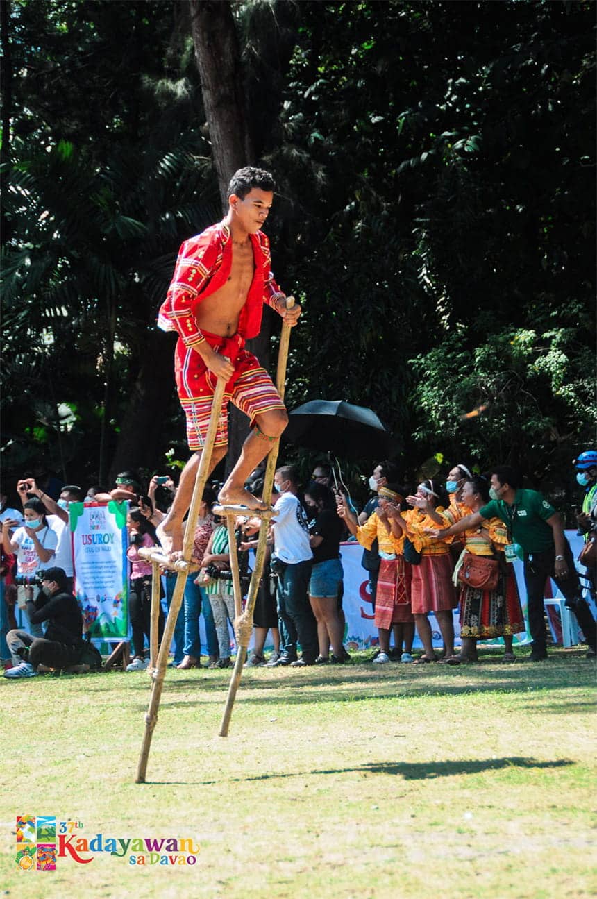 A young man on stilts in traditional attire performing at an outdoor cultural event.