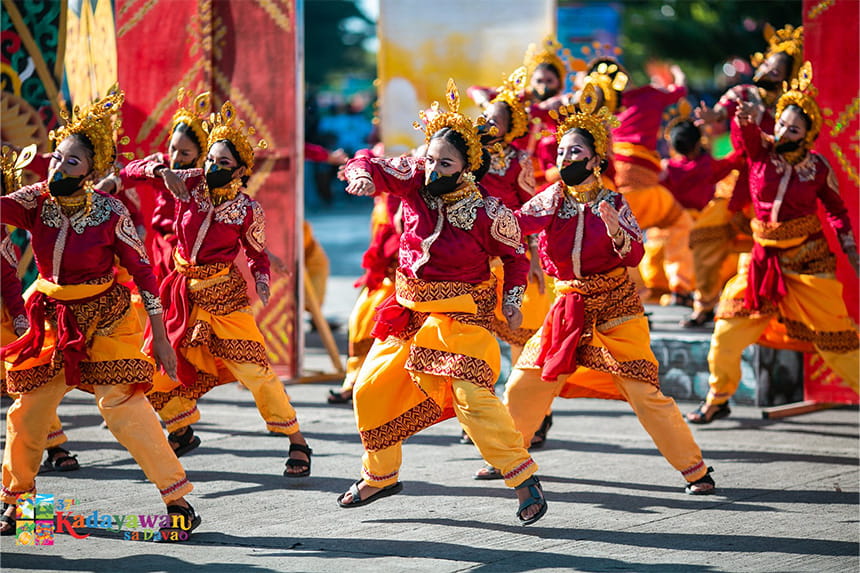 Dancers in traditional red and yellow costumes with gold headdresses performing outdoors.