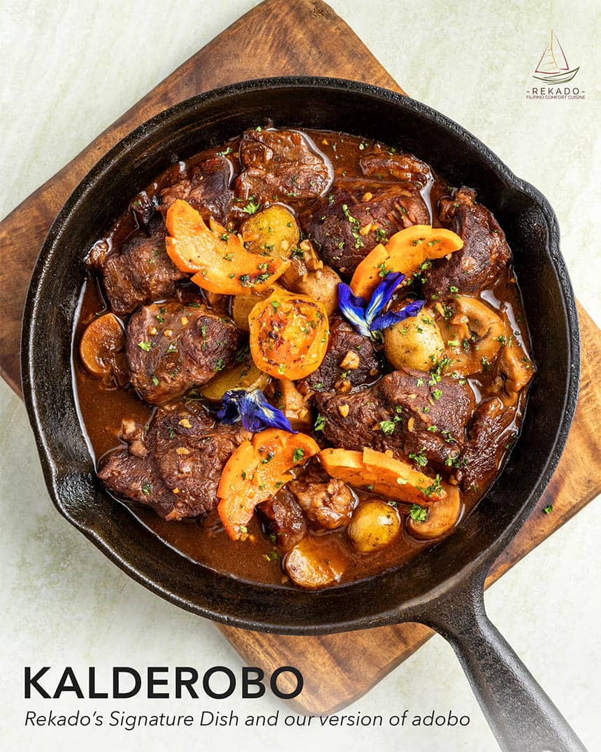 A dish of Kalderobo in a black skillet on a wooden board.