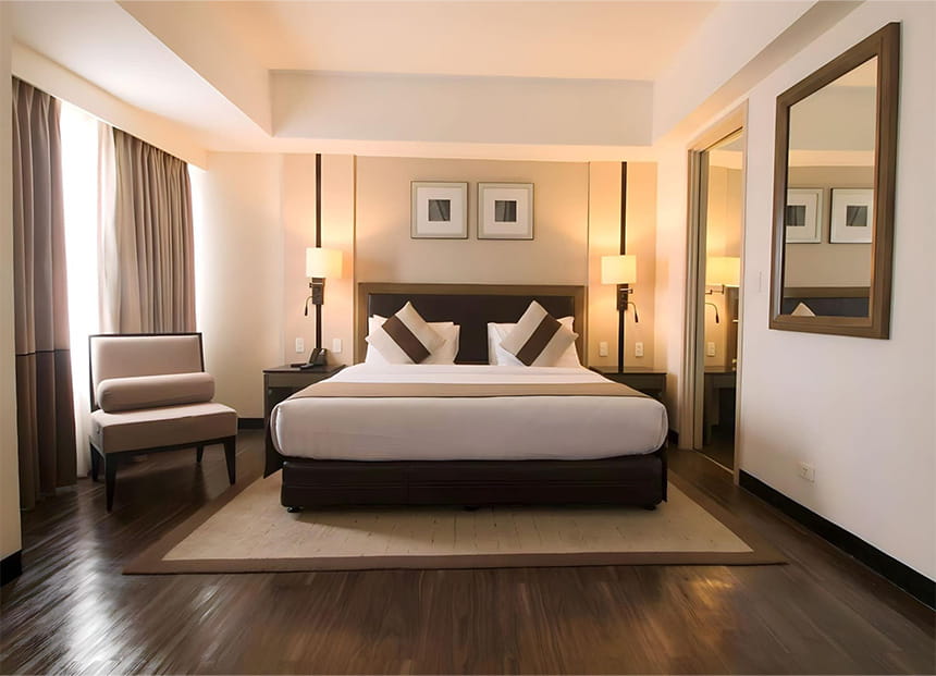 Modern hotel room with a large bed, bedside lamps, an armchair, and a mirror.