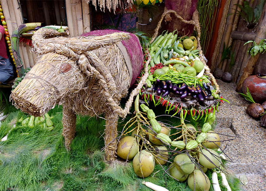 Straw buffalo sculpture with a cart full of vegetables and coconuts.