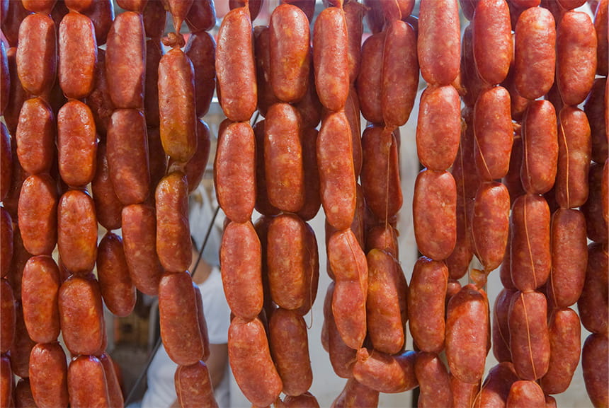 Rows of hanging reddish-brown sausages tied together with strings, forming a dense curtain.