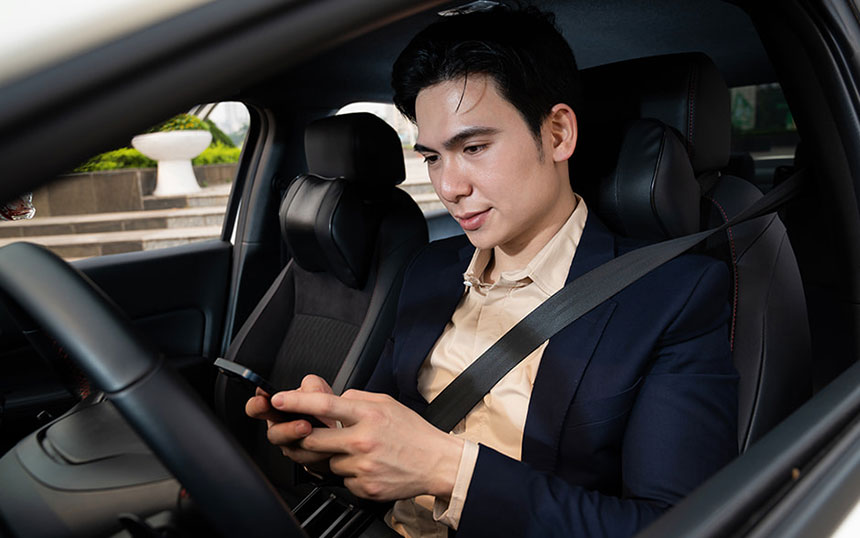 Businessman in a suit seated in a car, wearing a seatbelt and using his smartphone, symbolizing connectivity and multitasking while commuting.