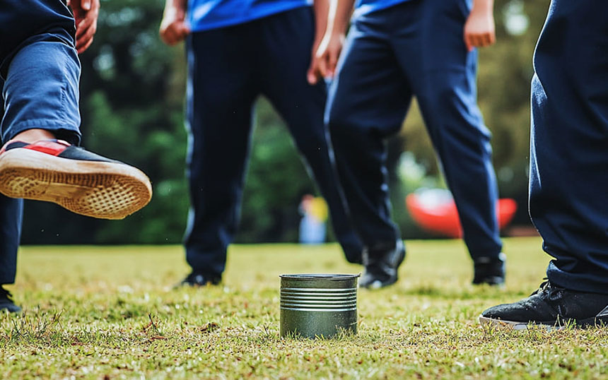 A dynamic shot of the traditional Filipino game 'Tumbang Preso,' capturing the moment a player kicks a tin can, surrounded by participants in blue athletic attire, set against a grassy outdoor field.