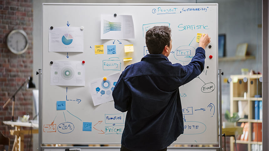 A man working on a whiteboard filled with notes, charts, and sticky notes in a modern office space.