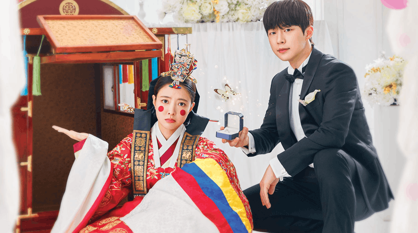 A man in a tuxedo kneels with a ring box, while a woman in traditional Korean attire looks surprised, sitting beside a colorful wedding palanquin in a bright, festive setting.