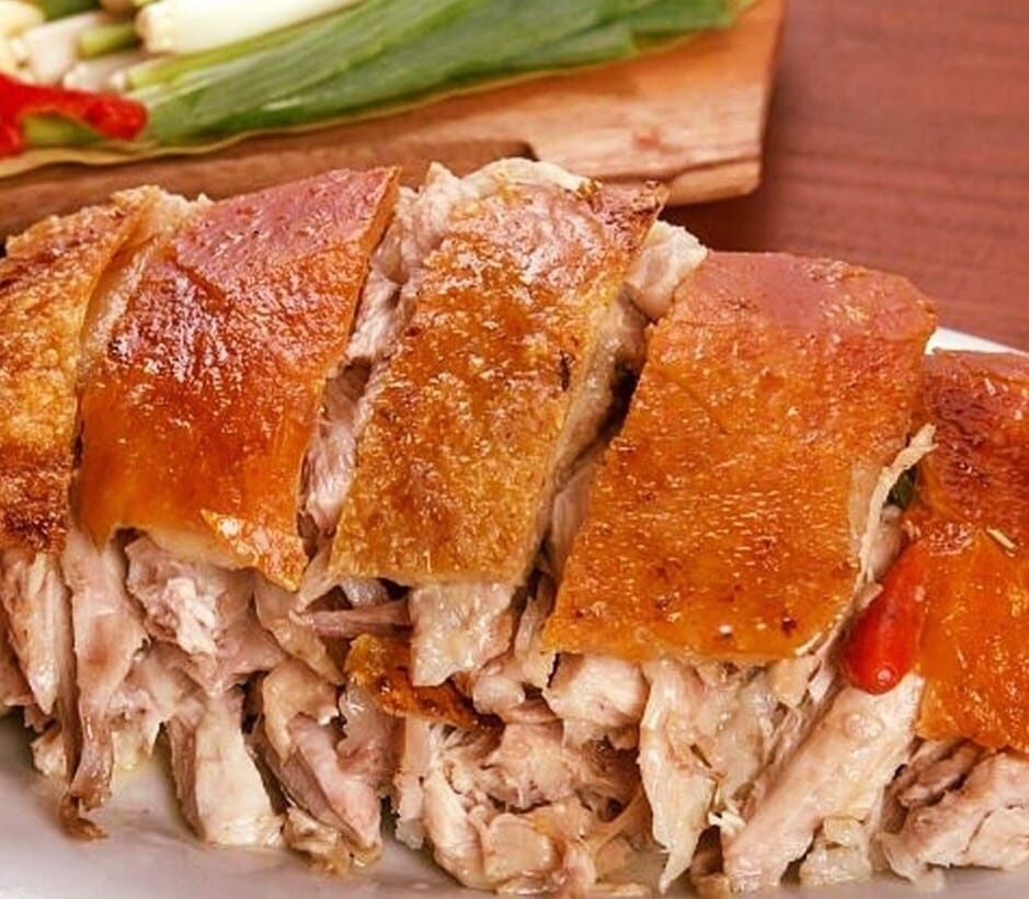 Closeup photo of sliced lechonâs crispy skin and tender meat against a wooden backdrop