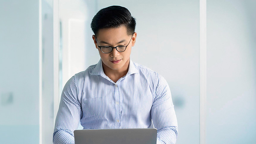A man wearing glasses typing on a laptop in an office.