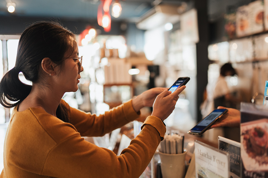 Woman using her smartphone while paying at a cashier.