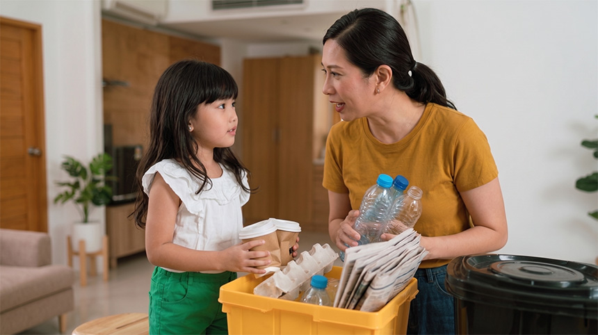 Adult and child sorting recyclable materials into a recycling bin at home.