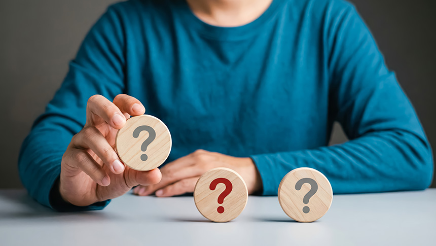 A person holding up a wooden disc with a question mark, with two more question mark discs on the table.