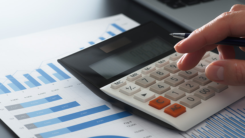 A person using a calculator over printed bar charts and financial reports.