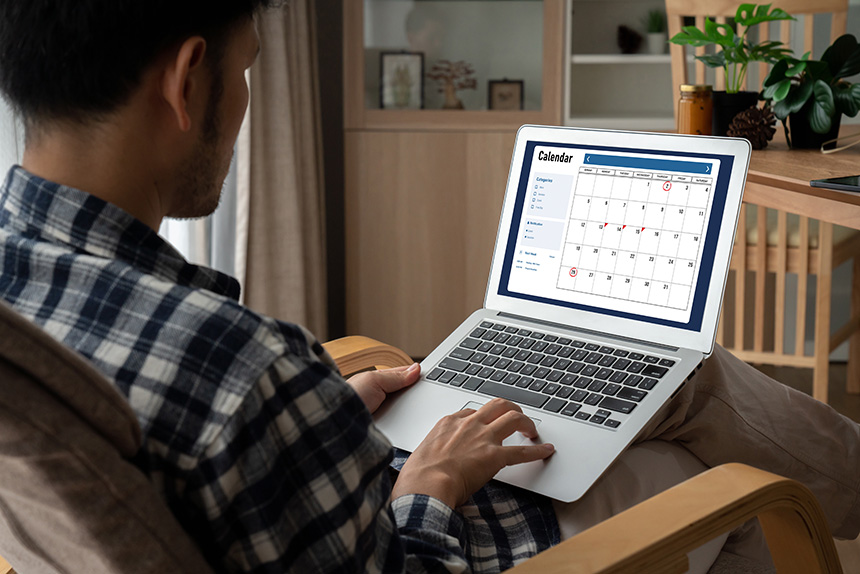 Photo of a man working on his laptop, using a calendar application.