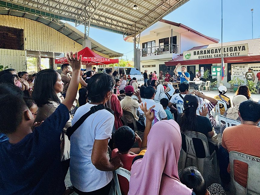 Residents raise their hands as a speaker addresses a community gathering outside Barangay Ligaya hall.