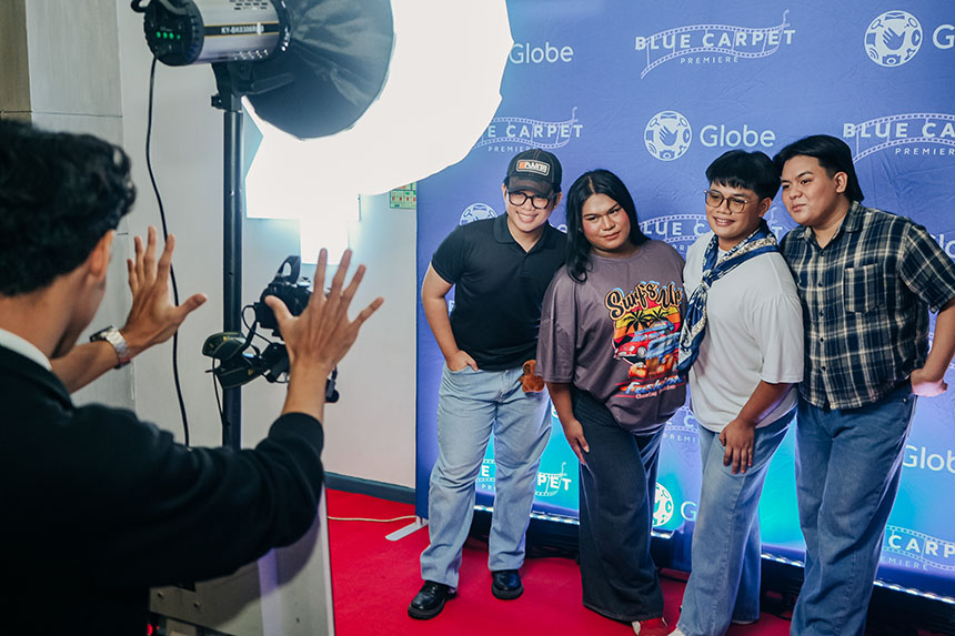 Behind-the-scenes shot of a photographer setting up a picture for four students standing on the blue carpet at a Globeâs movie premiere event.