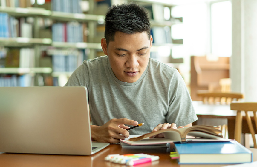 Male student, studying and reading a book in a library.