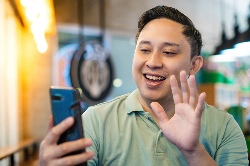 Asian man on a video call, waving.