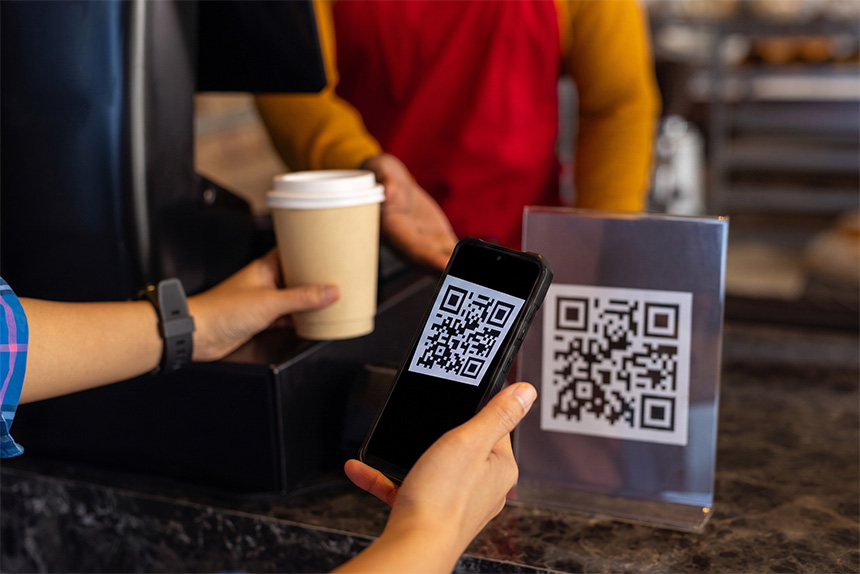 Close-up of hands holding a coffee cup and scanning a QR code at a counter, representing how GCash supports international cashless payments.