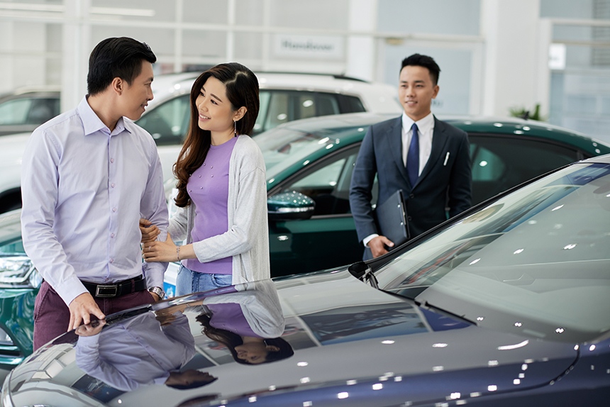 Photo of young Asian couple in a car dealership and looking at cars to buy.