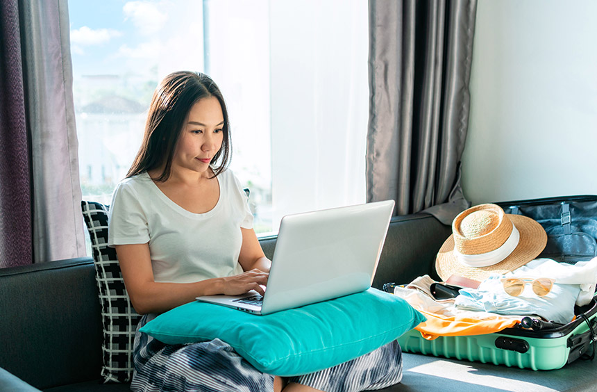 Traveler booking a trip on her laptop at home beside an open suitcase