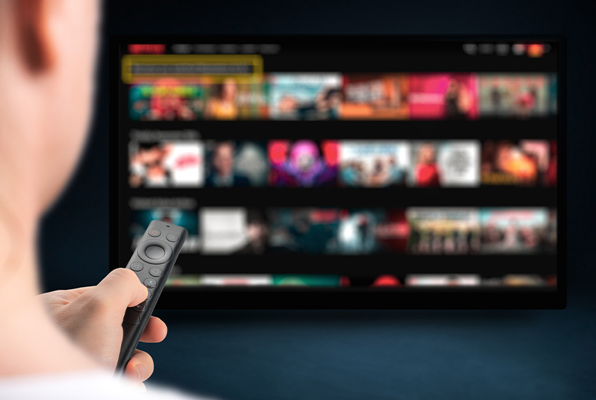 A person in front of a smart TV browsing titles with a remote.