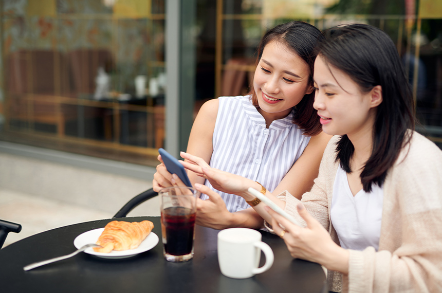 Two women using smartphones while sitting at a café.