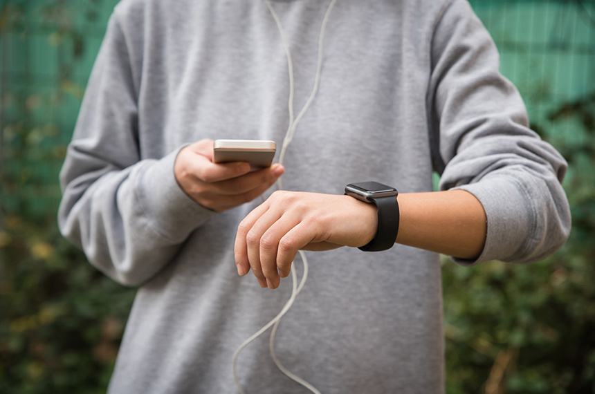 Person checking a smartwatch while holding a smartphone outdoors.