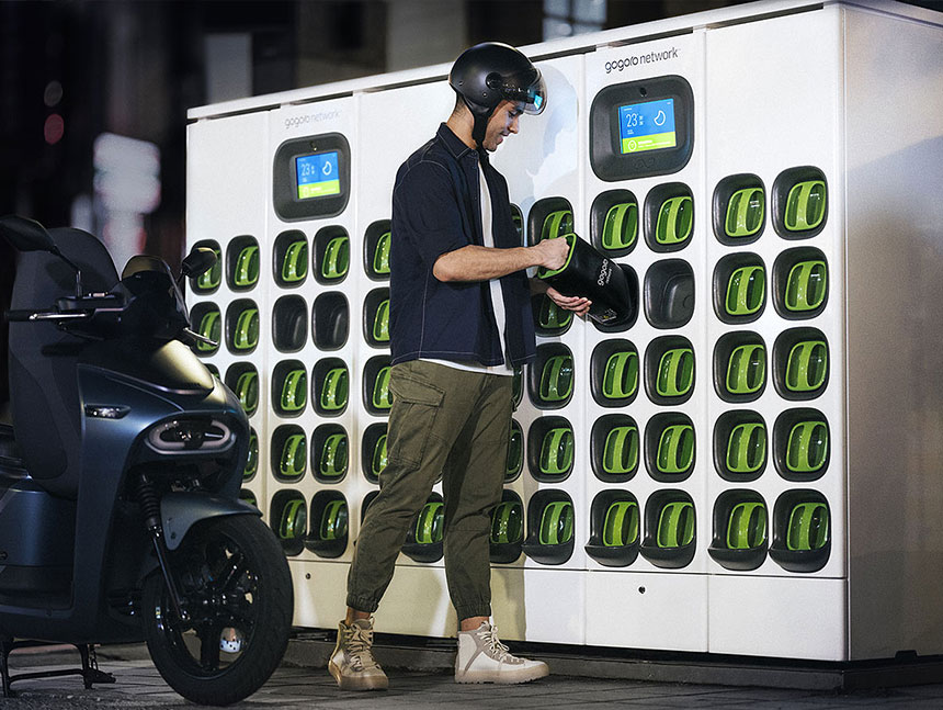 Person swapping a battery at a Gogoro charging station beside an electric scooter