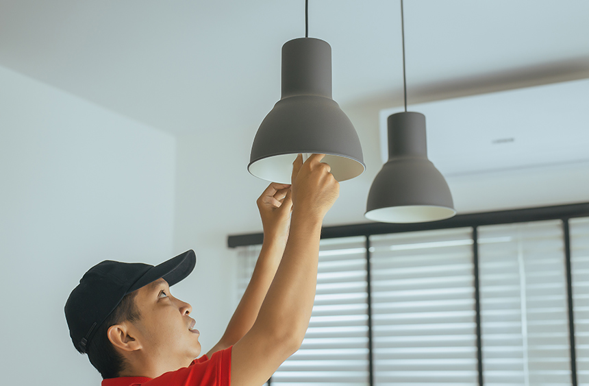 Text: Asian man changing a light bulb at home.