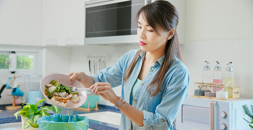 Young Asian woman scraping food leftovers into a bin.