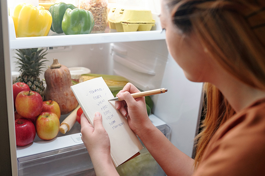 Person making a grocery list at the refrigerator.