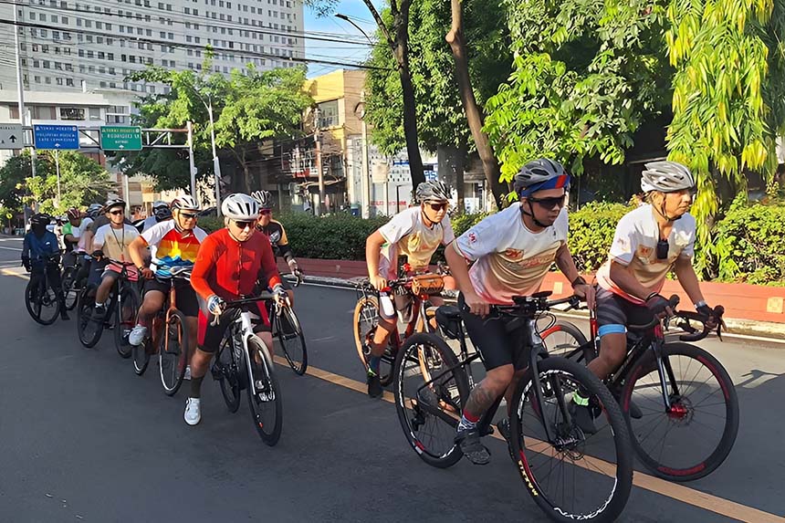 A group of cyclists riding together down a city street on a sunny weekend.