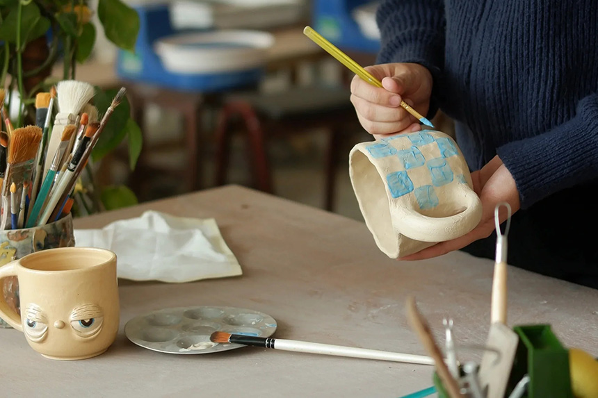 Individual working intently on a pottery piece, painting over their artistic creation.