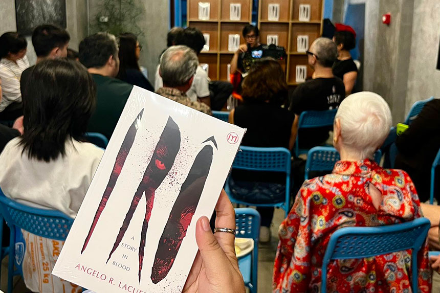 A person raises a copy of Sarge Lacuestaâs newest book, Irô: A Story in Blood, in front of an engaged crowd.