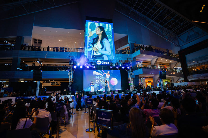 Alex Eala on stage at her Globe homecoming fan meet in Manila, surrounded by a large crowd of fans.