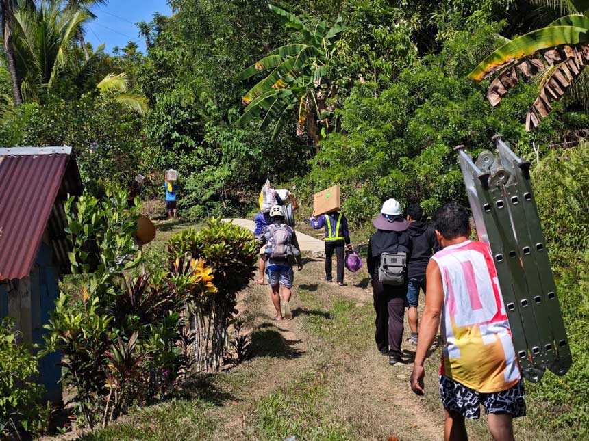 Globe personnel hiking with telecommunications equipment to a remote site for the DICT Bayanihan SIM Project.