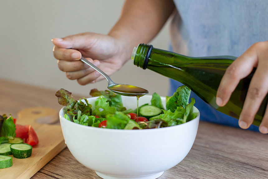Olive oil being poured over a fresh salad, a staple of the Mediterranean Diet.