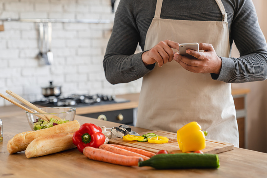 Person using a smartphone while preparing vegetables in the kitchen.