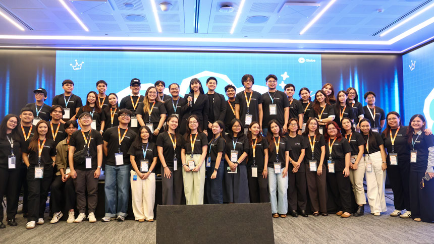 A group photo of 40 student interns wearing black polo shirts and lanyards, smiling and posing together on a stage with a blue Globe-branded backdrop.