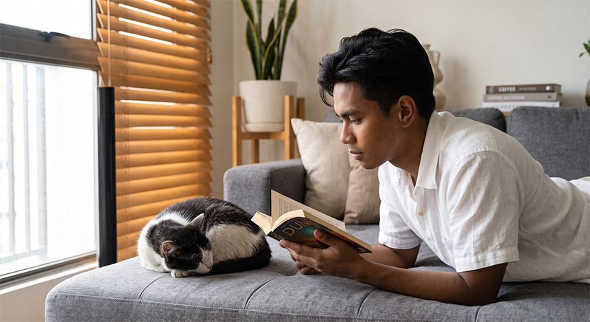 Man spending quiet time reading beside his cat.