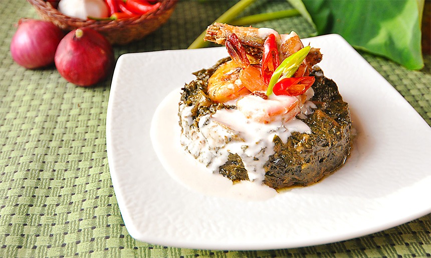 Chef Doy's laing with rich, creamy coconut milk topped with shrimp on a white plate on top of a green tablecloth.