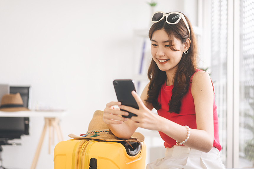 Woman using her smartphone beside a suitcase while preparing to travel.